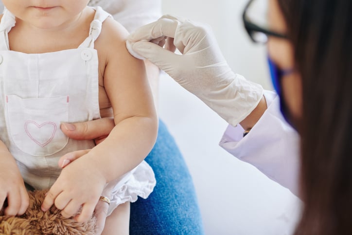 Doctor in rubber gloves wiping injection site on arm of little girl before vaccinating her