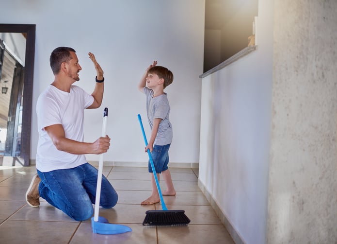father and his little son with autism high fiving each other while sweeping the floor at home