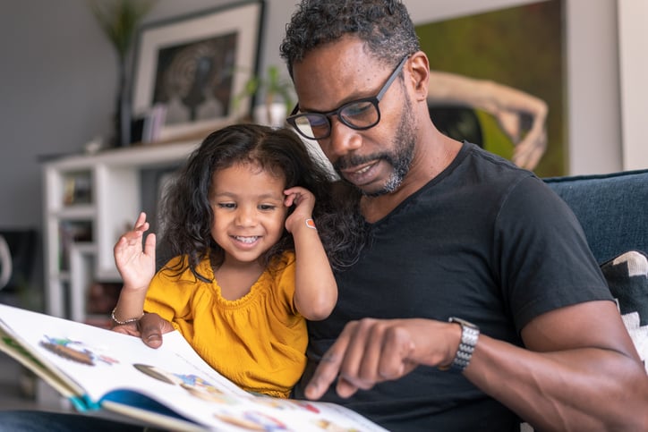 Father on the couch at home reading a storybook to his preschool age daughter with autism