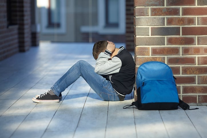 autistic boy sitting on the ground covering his ears due to loud noise at school