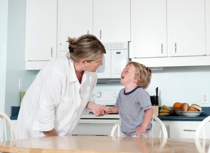 mother trying to calm her crying toddler with autism at home in their kitchen