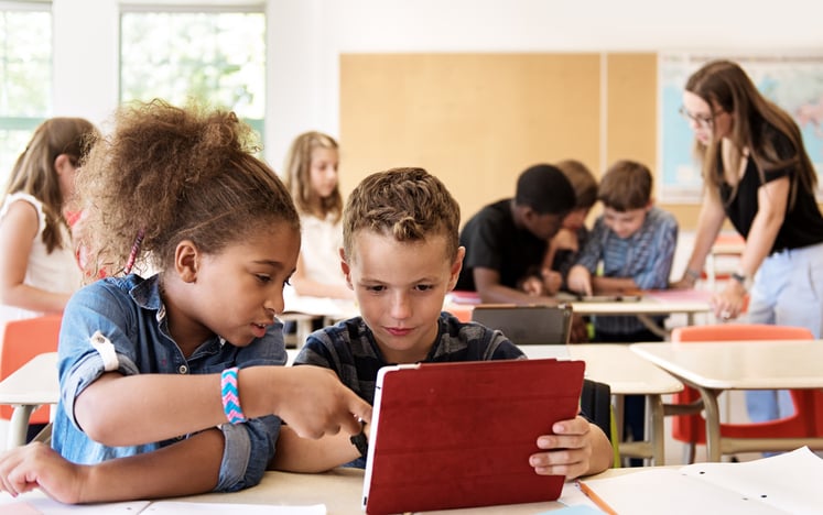 School kids in class using a digital tablet with one helping the other