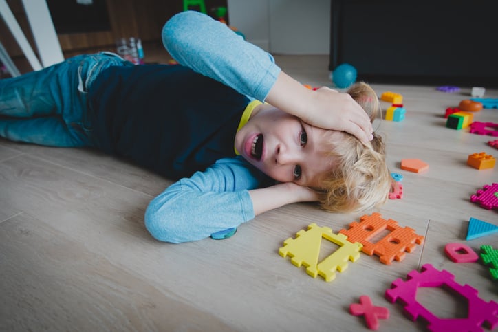 young autistic boy shouting with toys scattered around